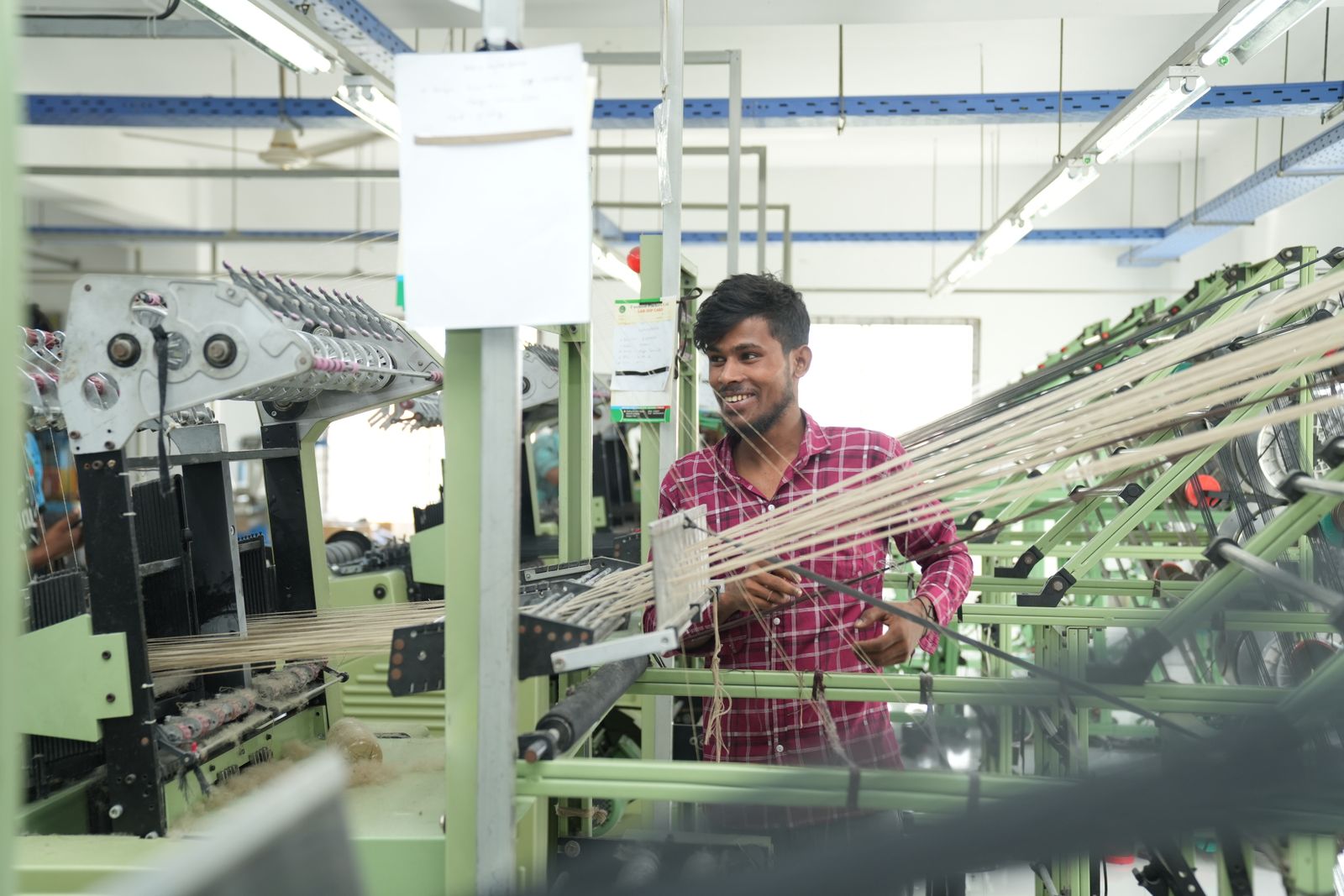 Bangladeshi textile worker operating machines on a bright factory floor